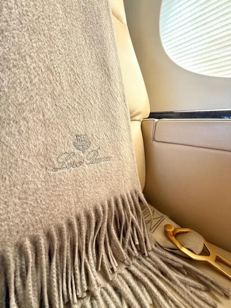 Close-up of a Loro Piana blanket on a beige leather seat in the aircraft cabin.