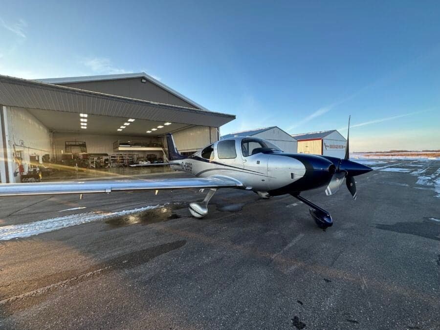 A Cirrus aircraft is parked outside a hangar on a sunny day.