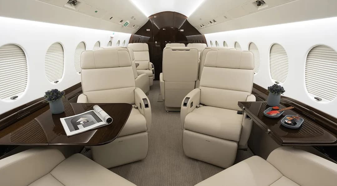 The aircraft interior features cream-colored leather seats and wood tables with decorative items.