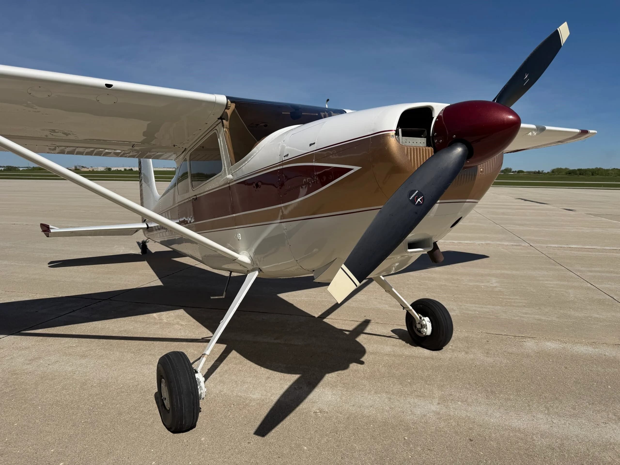 Front-right view of a white, gold, and maroon Cessna 172 on an airfield.