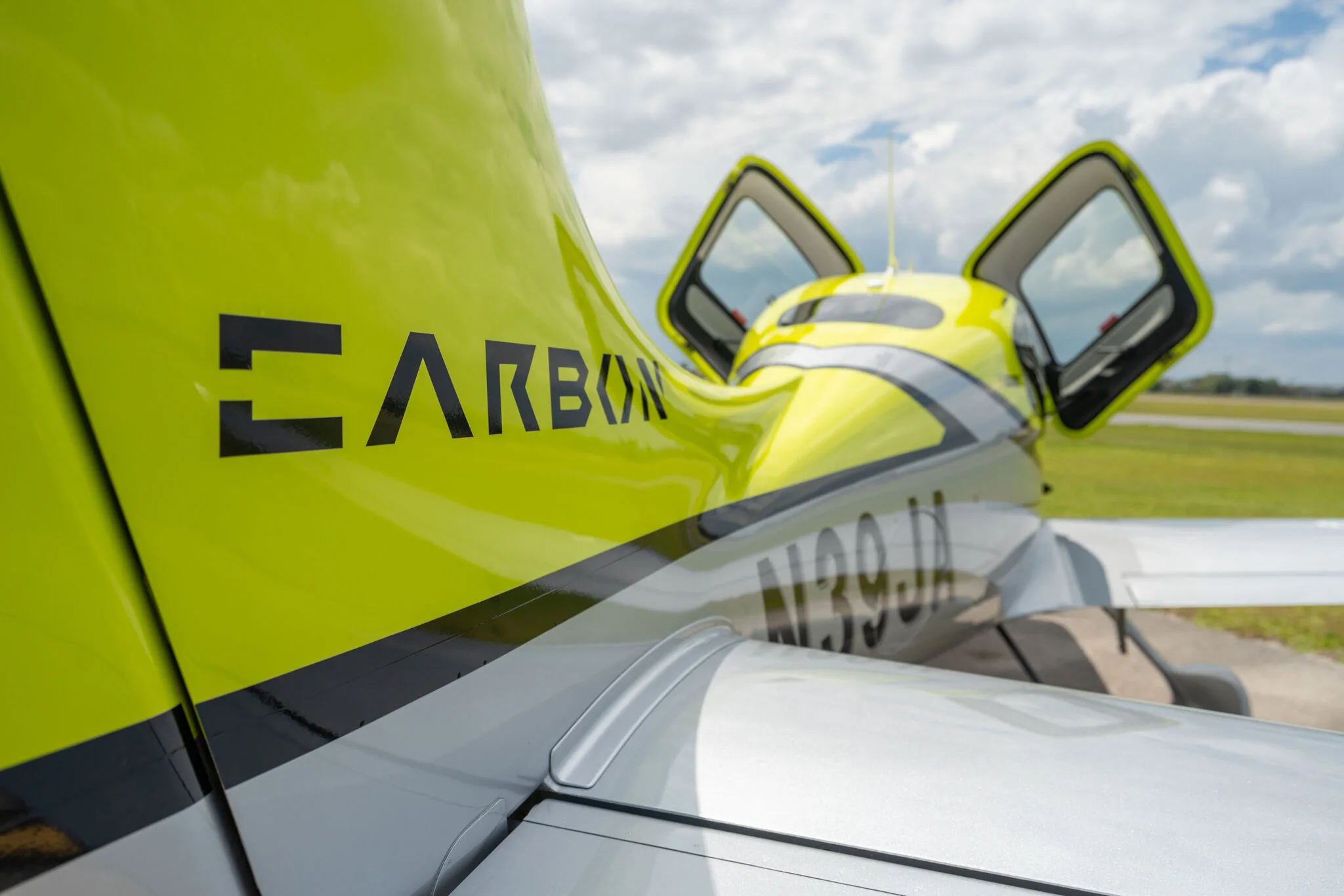 Rear view of a lime green and silver Cirrus SR20 aircraft with open cabin doors, showing the "CARBON" decal on the tail.