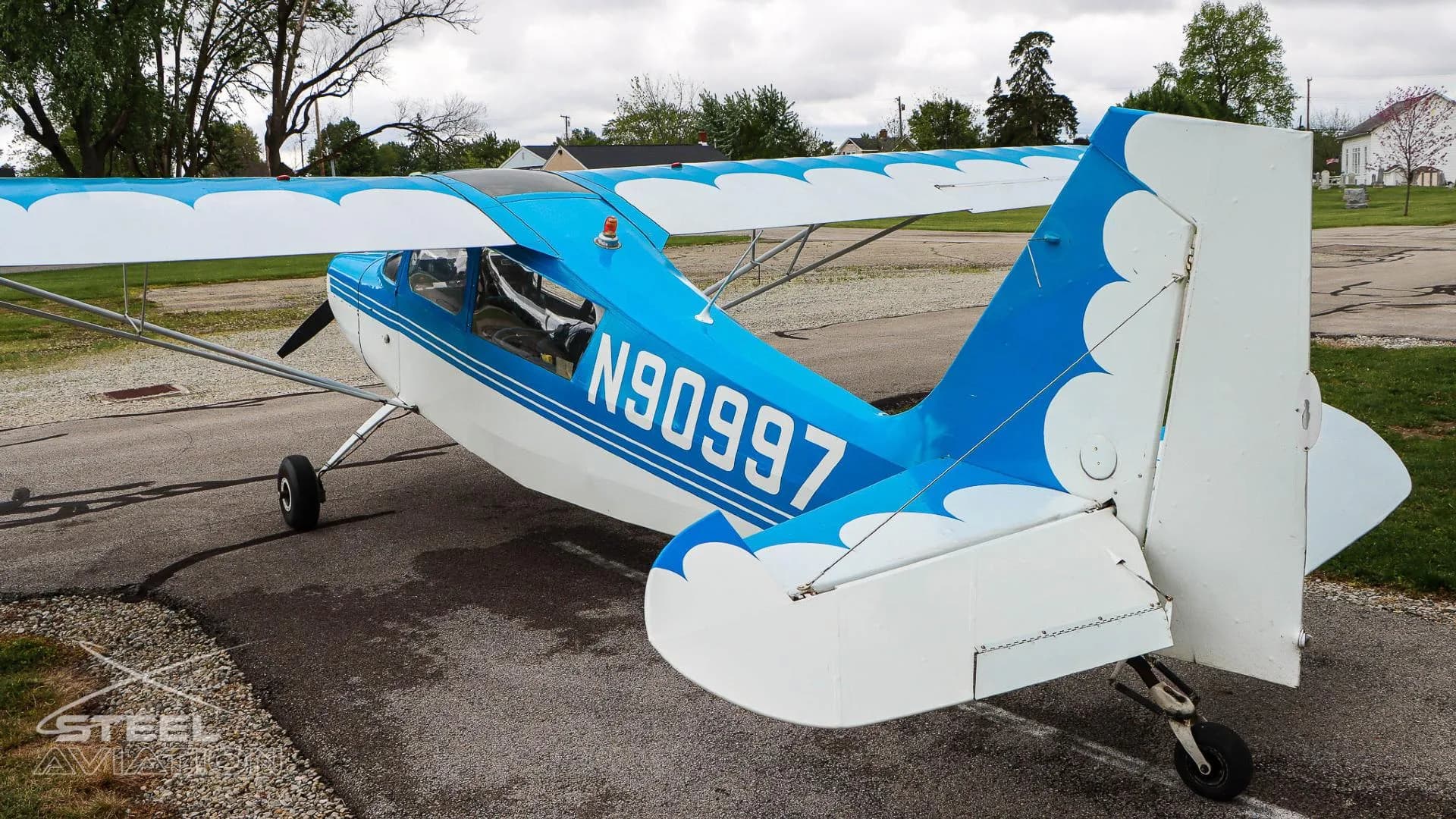 Rear three-quarter view of a white and blue Bellanca 7GCBC Citabria aircraft with registration N90997, showing the tail and right wing.
