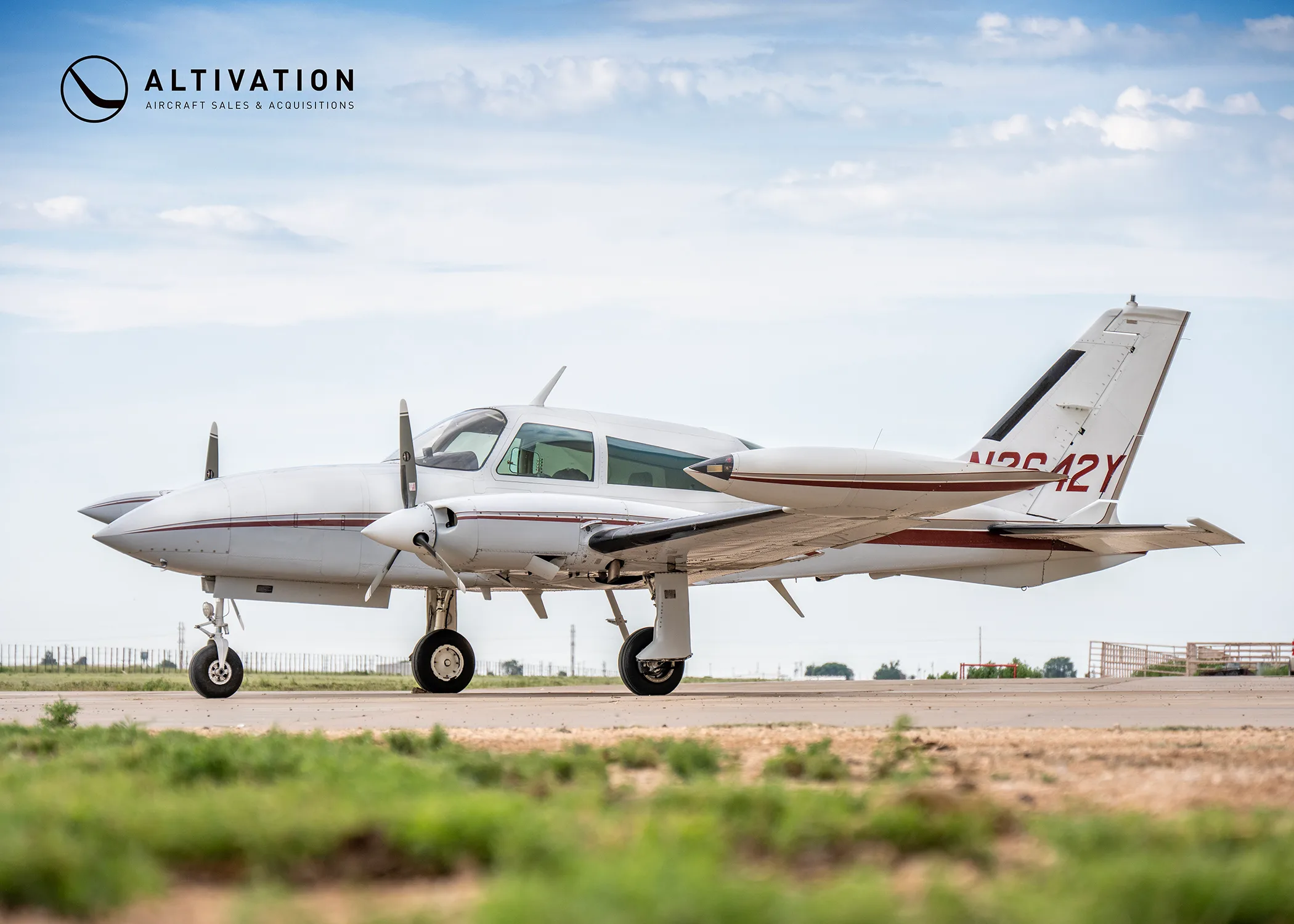 A white twin-engine propeller aircraft with maroon stripes, tail number N2642Y, parked on an airfield.
