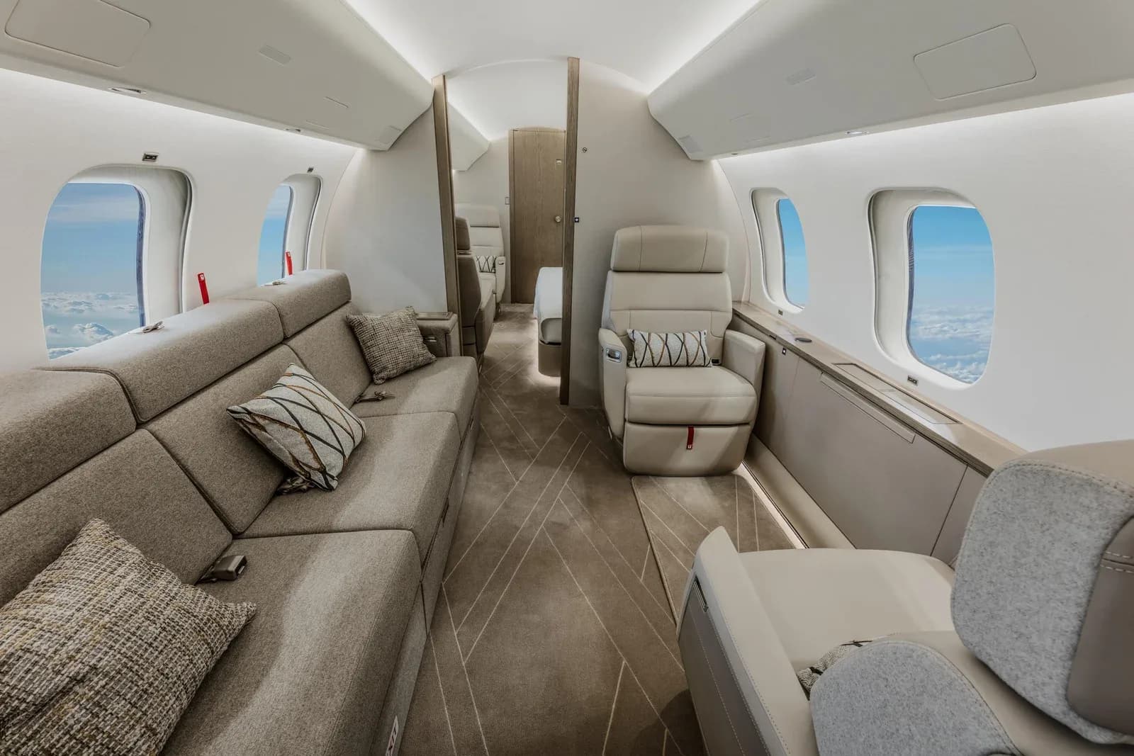 The business jet cabin interior featuring a long grey sofa with throw pillows and a single light-colored armchair.