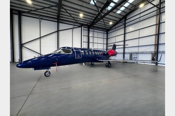 A dark blue Bombardier Challenger 350 business jet is parked inside a large, well-lit hangar.