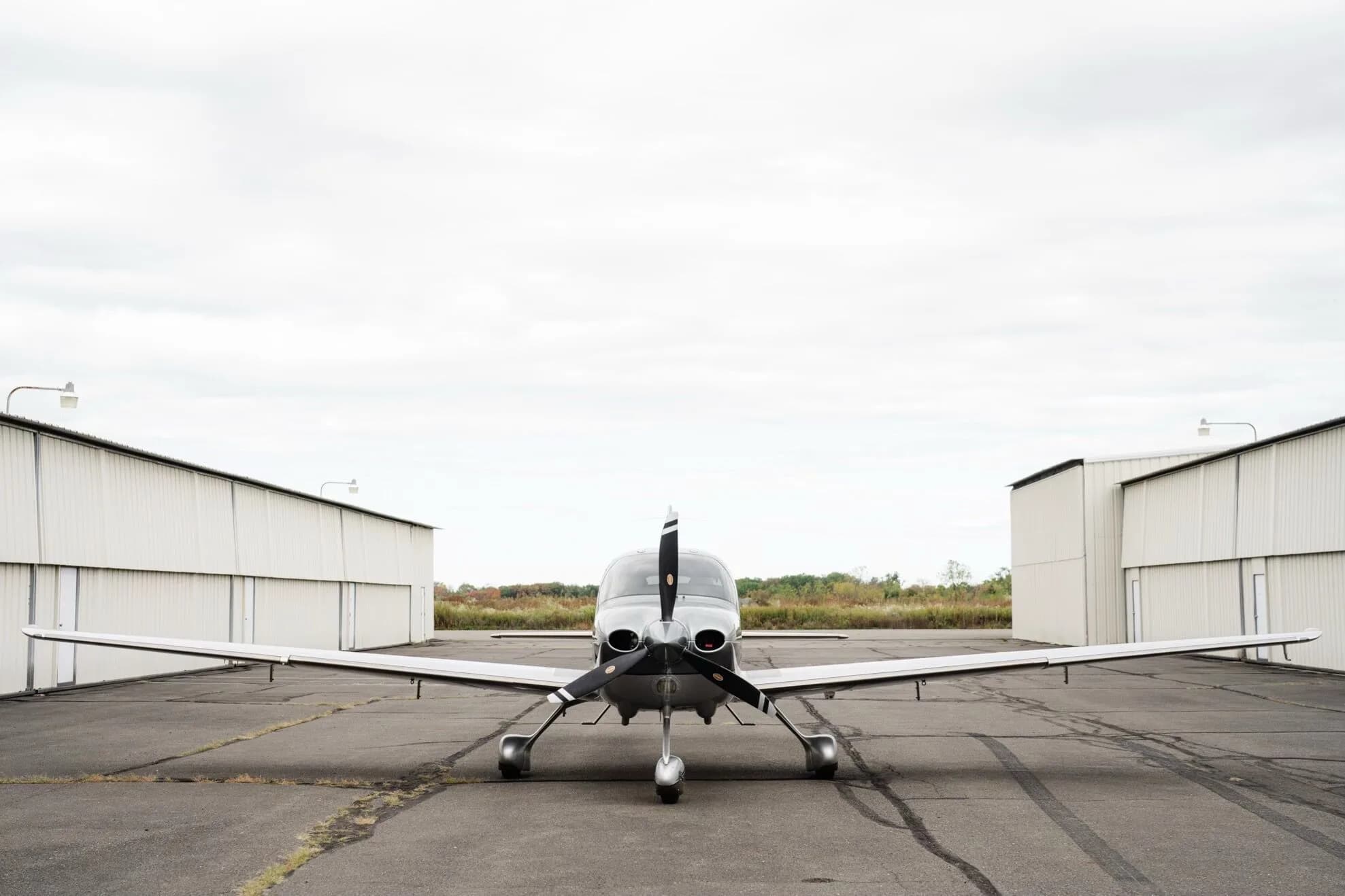 A head-on view of the silver Cirrus SR22 GTS Platinum aircraft, N424AX, parked between two hangars.