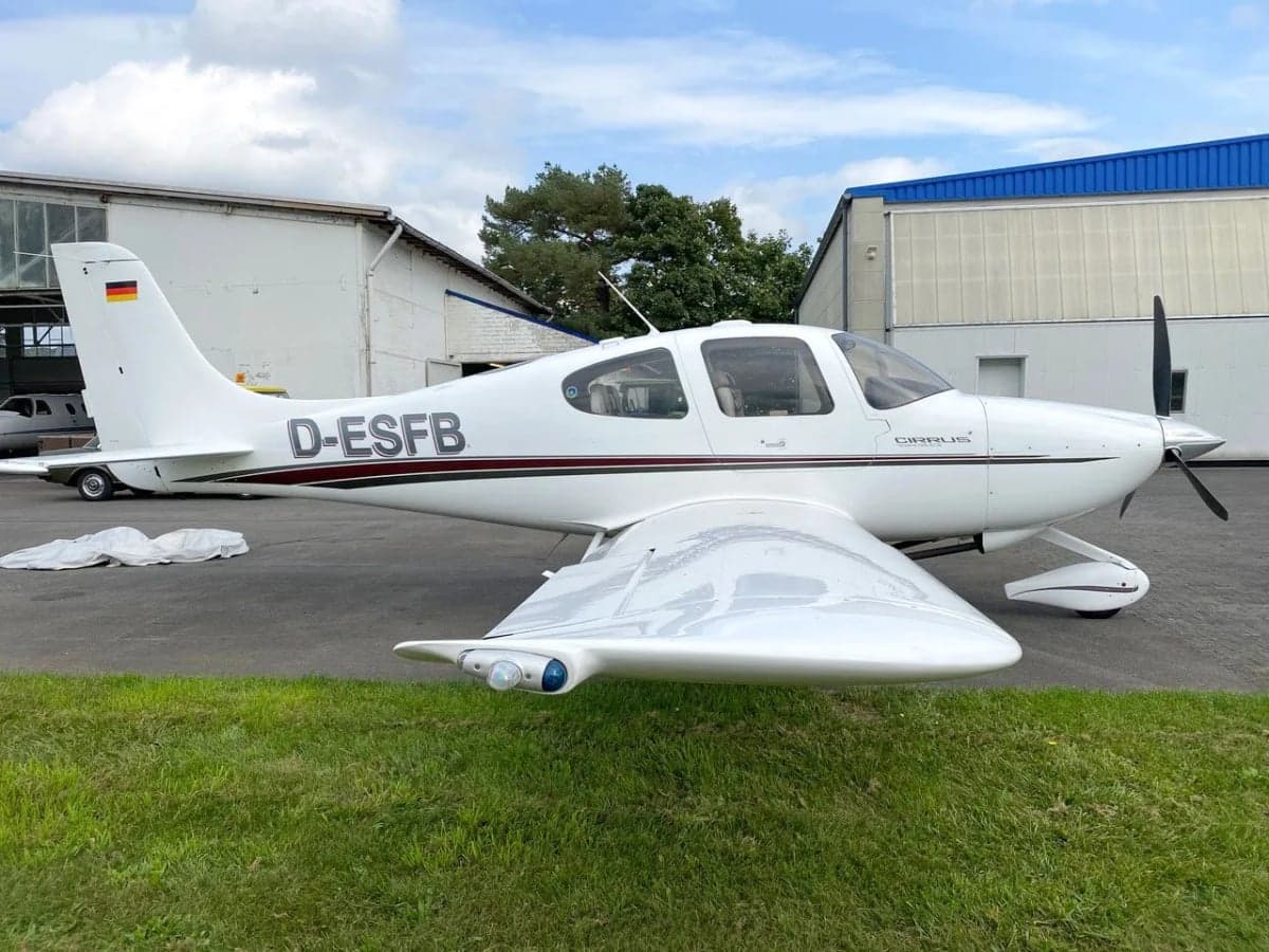 Cirrus aircraft D-ESFB parked on the grass in front of a hangar.