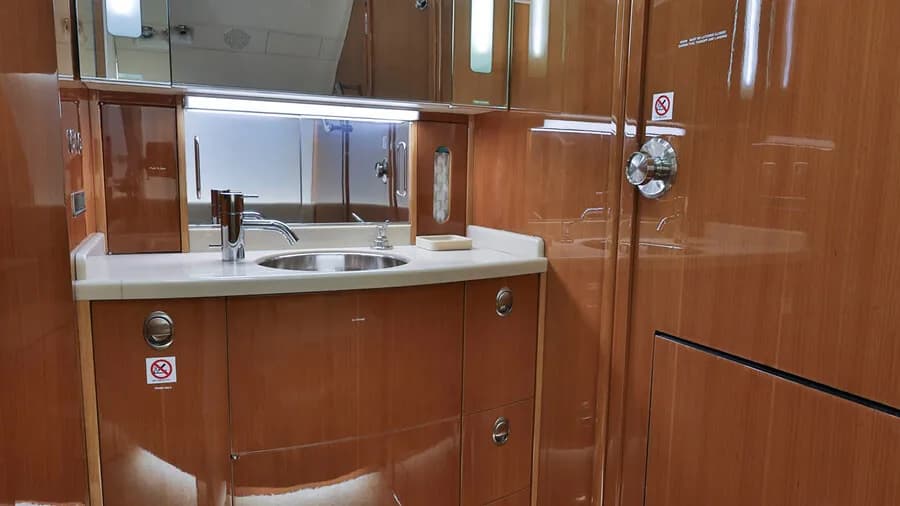 A private jet lavatory with a sink, mirror, and polished wooden cabinetry.
