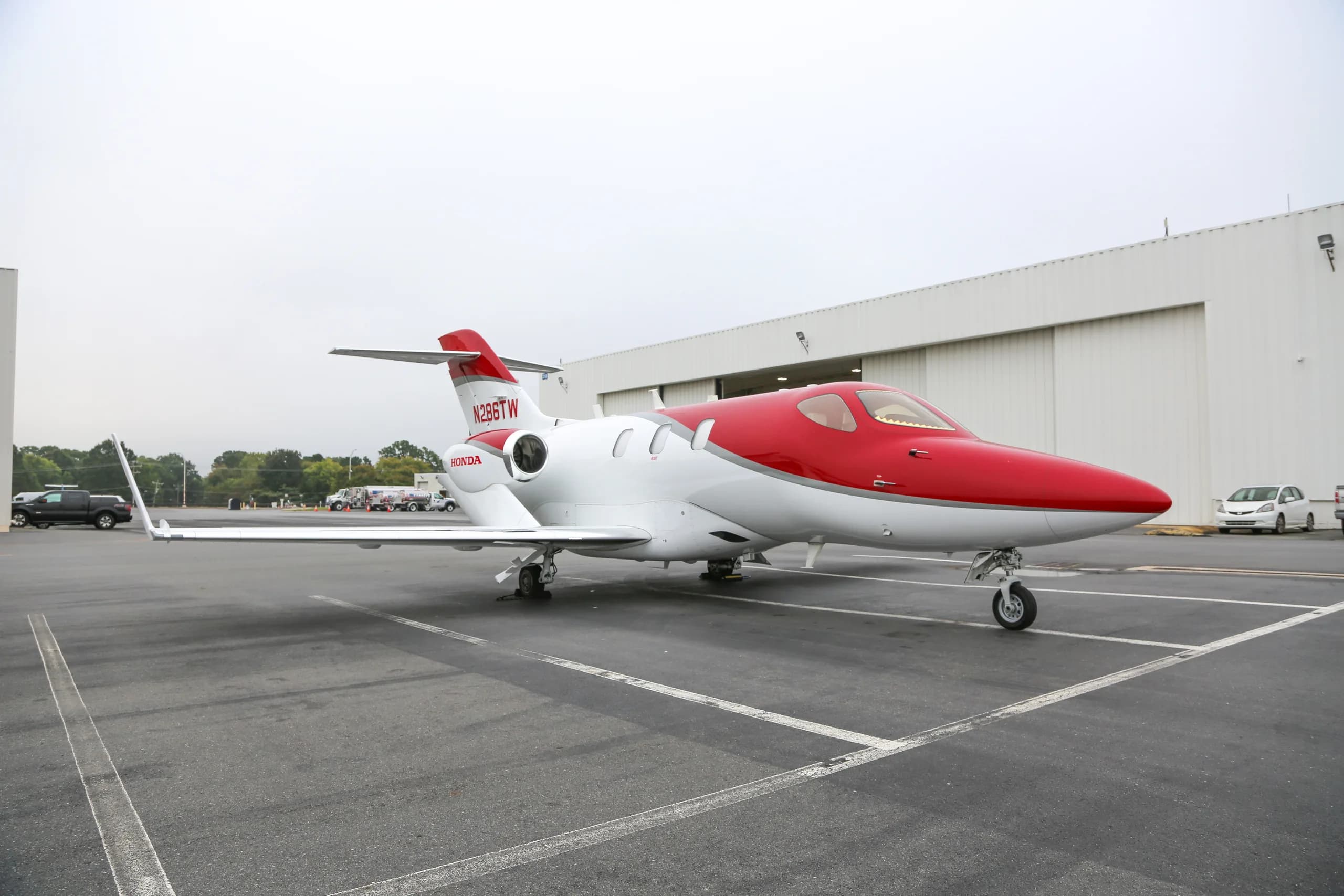A white and red HondaJet, registration N286TW, parked on an airport tarmac in front of a hangar.