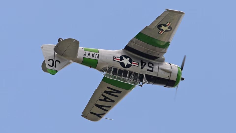 Underside view of a silver and green T-6 Texan aircraft in flight.