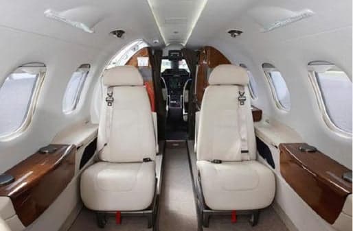 Aircraft interior with white leather seats and wood trim.