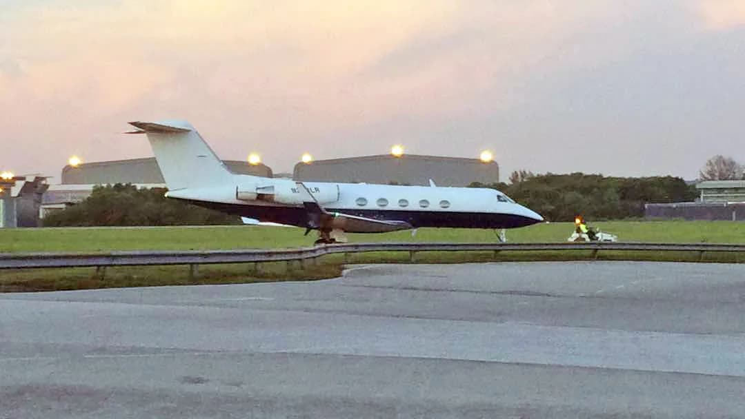 A Gulfstream G-IV business jet, registration N234LR, in a white and dark blue paint scheme, taxiing on a tarmac at dusk.