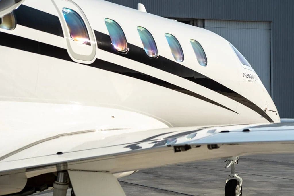 Close-up of the side of a Phenom 300 aircraft, showing the windows and wing.