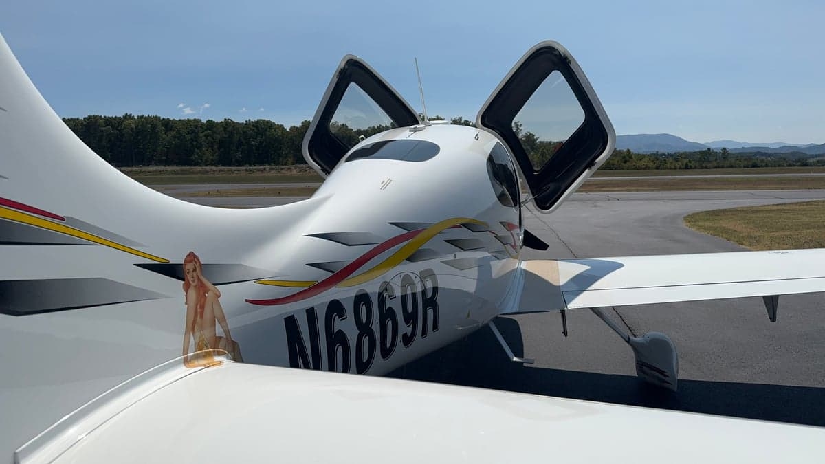 Rear view of a Cirrus aircraft with its doors open, showing the registration number N6869R and custom graphics.