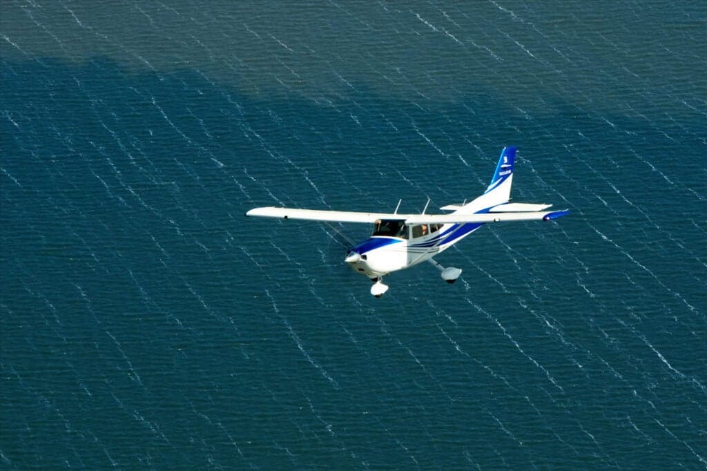 A Cessna Skylane flying over water.