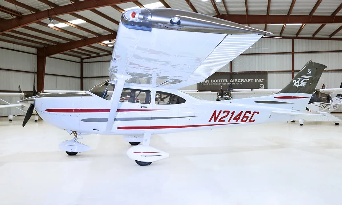 A side view of a white Cessna 182 Skylane with red and grey stripes, registration N2146C, parked in a hangar.
