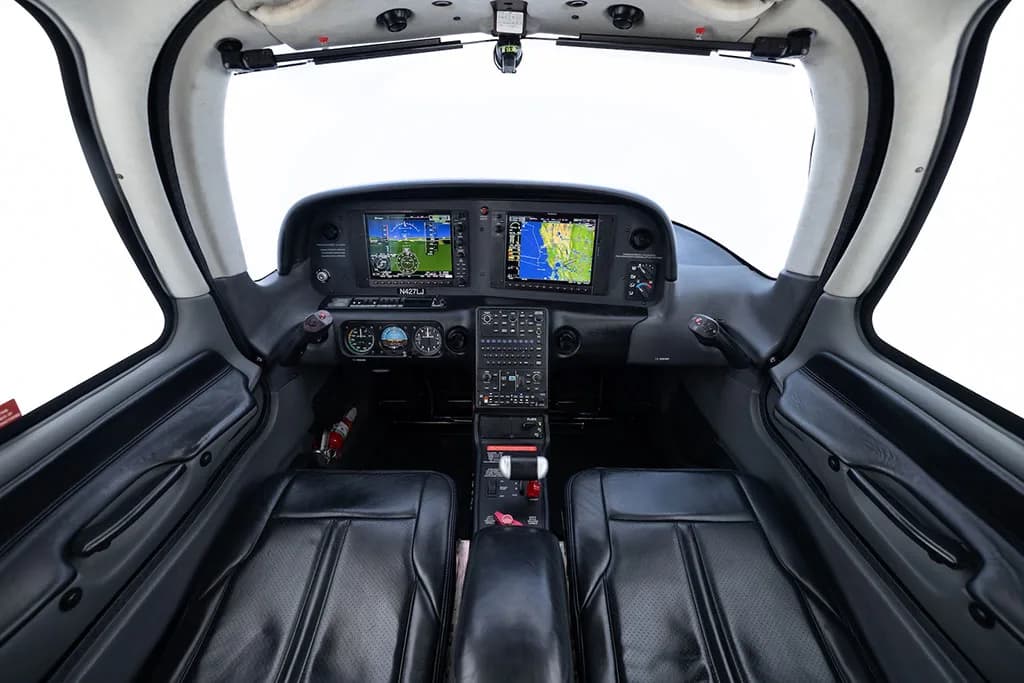 View of the aircraft cockpit with two black leather seats and a modern glass panel display.