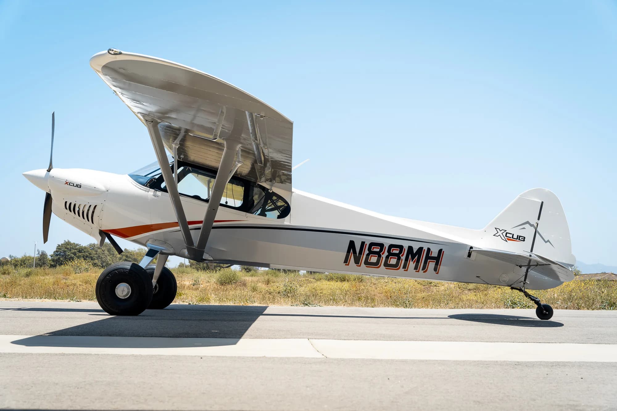 A white and gray CubCrafters XCub, registration N88MH, is parked on the tarmac.