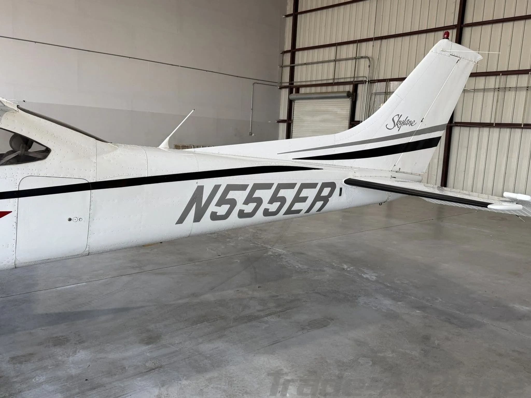 A close-up view of the tail section of the white Cessna 182 Skylane, showing the N-number and "Skylane" script, inside a hangar.