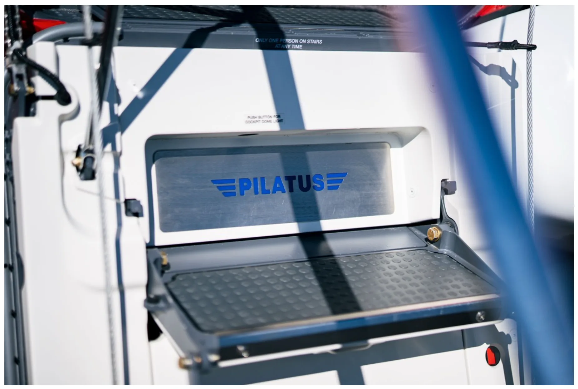 A close-up of the open airstair door of a Pilatus aircraft, showing the blue "PILATUS" logo on the interior panel.