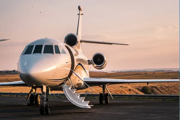 A white business jet with its door open and stairs deployed, parked on an tarmac at sunset.