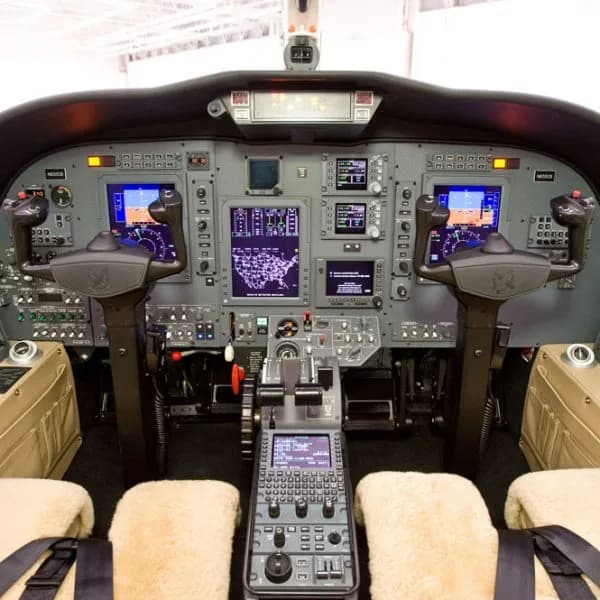 The cockpit of a private jet, featuring multiple digital displays, control yokes, and a central control panel.