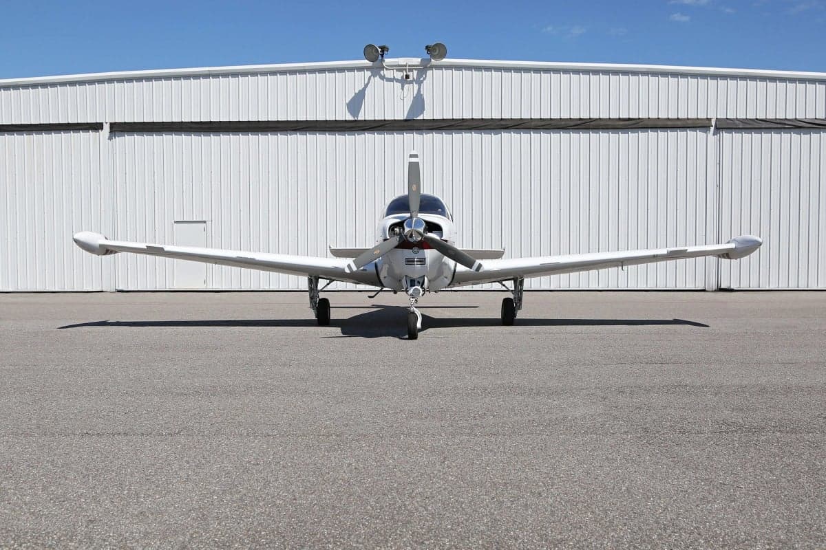 Front view of a white and red Beechcraft Bonanza aircraft parked in front of a hangar.