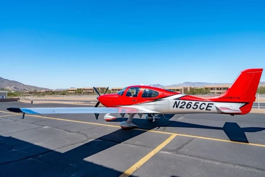 A three-quarter side view of the red and silver Cirrus SR22T GTS Carbon aircraft, registration N265CE, parked on an airfield.