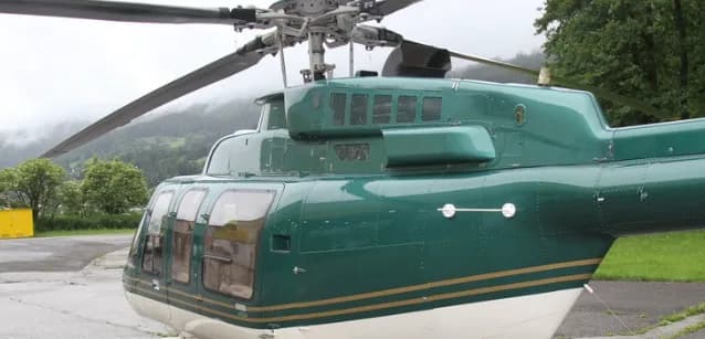 A close-up of the Bell 407 helicopter's fuselage shows the green and white paint scheme.