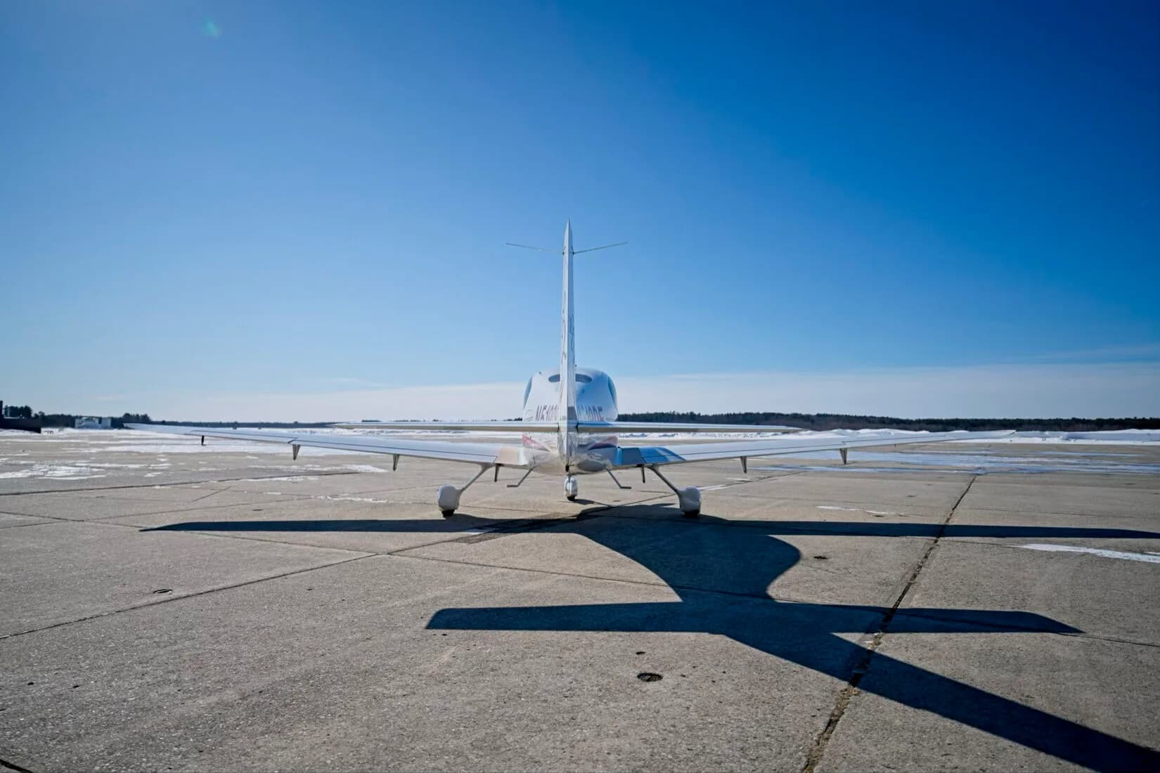 A rear view of a white Cirrus SR22 aircraft with its tail facing the camera, parked on a tarmac.
