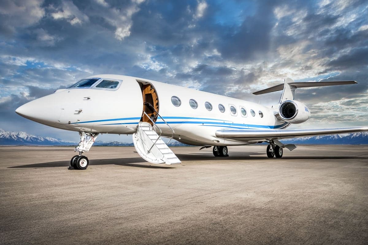 A white and blue Gulfstream business jet is parked on the tarmac with its door open.