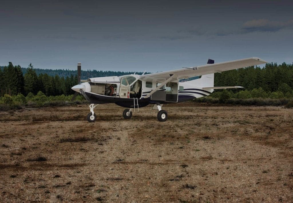 A Cessna Caravan parked on a dirt airstrip with the doors open.