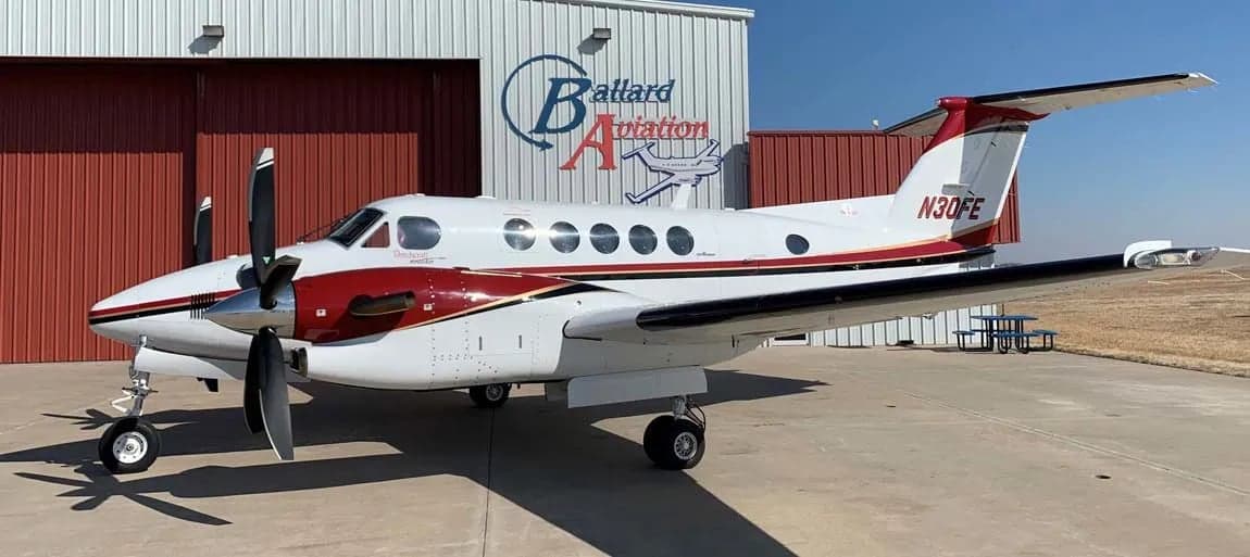 A Beechcraft King Air 200 with registration N30FE parked on the tarmac in front of a hangar.
