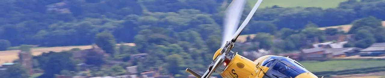 Close-up of a yellow and blue helicopter in flight over a rural landscape.
