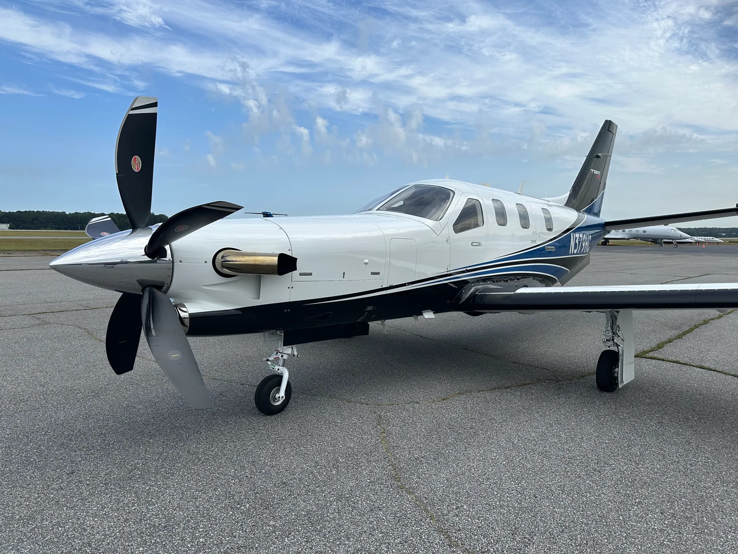 A white and blue TBM 960 turboprop aircraft with its propeller visible, parked on an asphalt tarmac.
