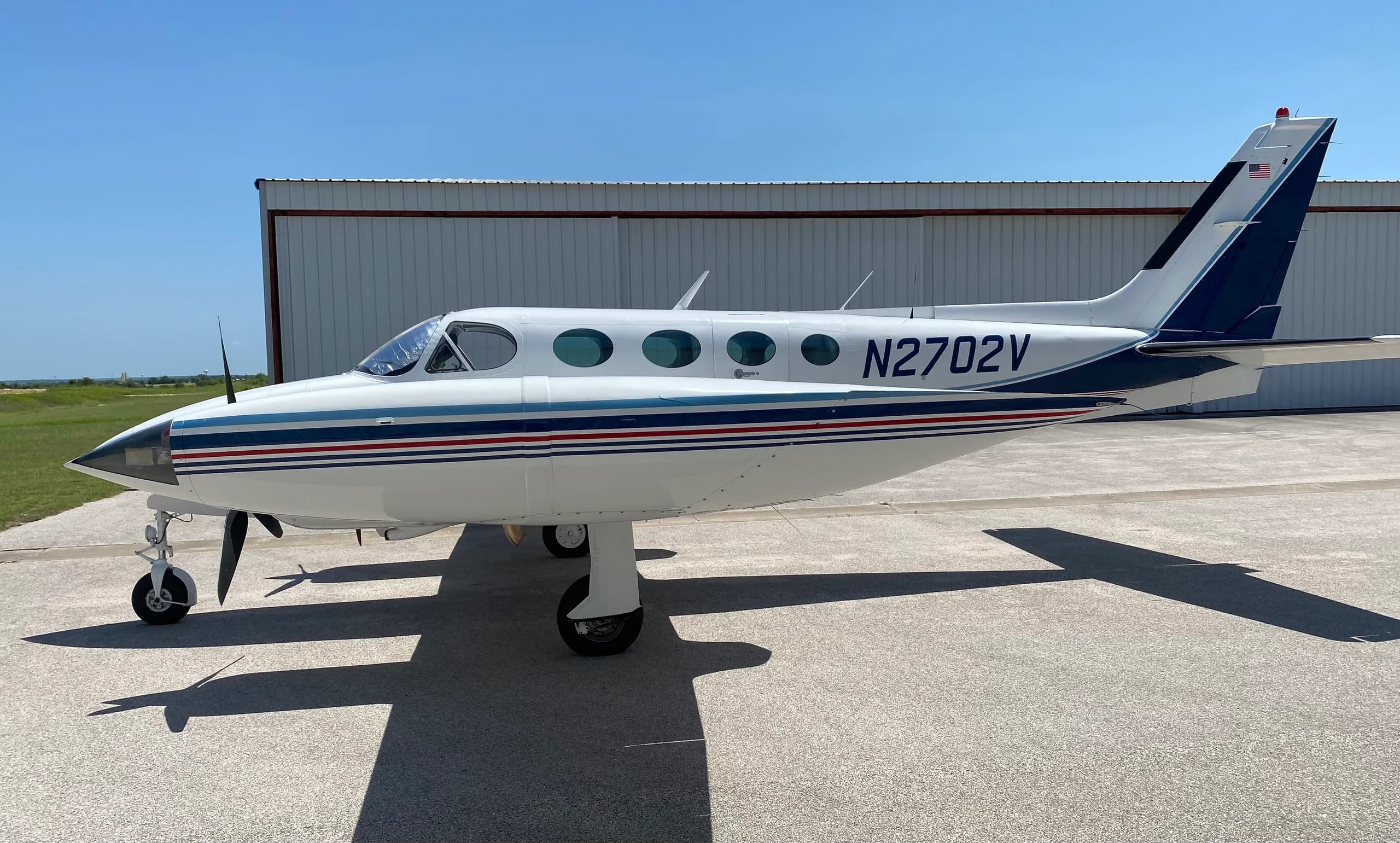 A Cessna 340A aircraft with registration N2702V parked on the tarmac, side view.