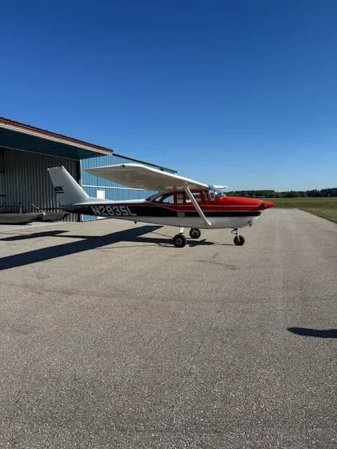 A red and white Cessna 172, registration N2835L, parked on an asphalt apron next to a blue hangar under a clear blue sky.