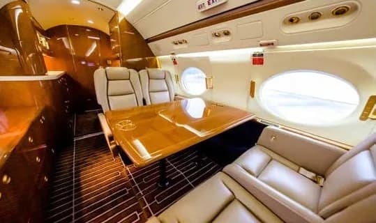 Interior of a private jet with leather seats and a wooden table.