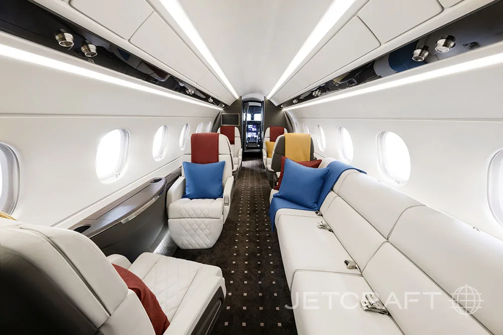 The interior of a jet aircraft with white leather seats and blue pillows.