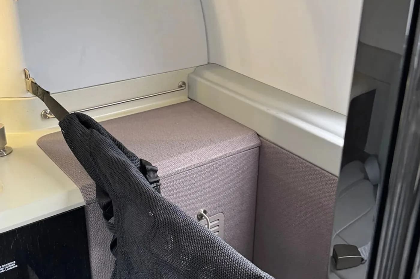 A detailed view of an aircraft interior storage compartment or lavatory area with a dark mesh bag hanging.