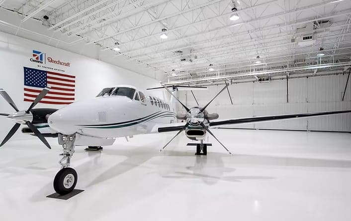 A Beechcraft King Air 360 is parked inside a hangar with an American flag in the background.