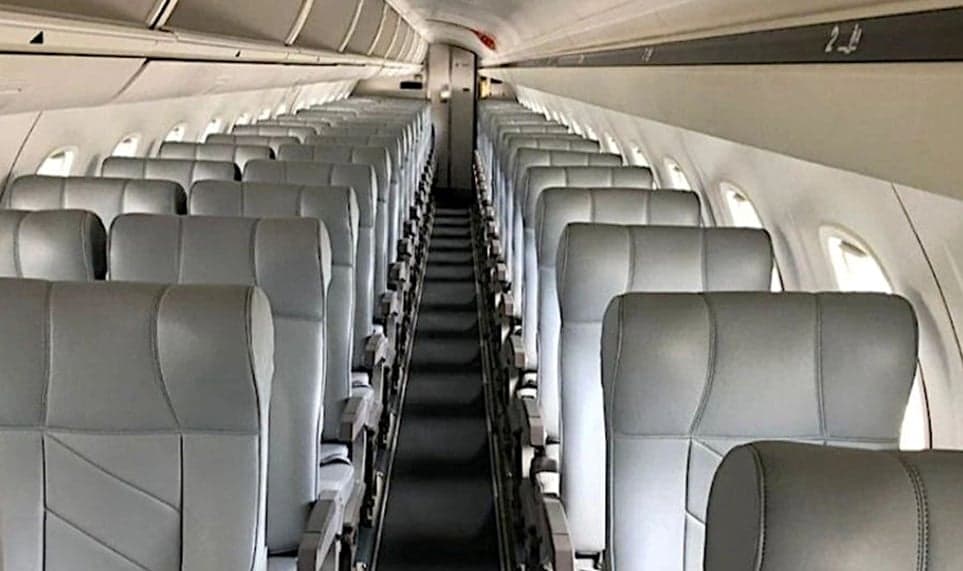 View down the aisle of an Embraer cabin with grey leather seats.