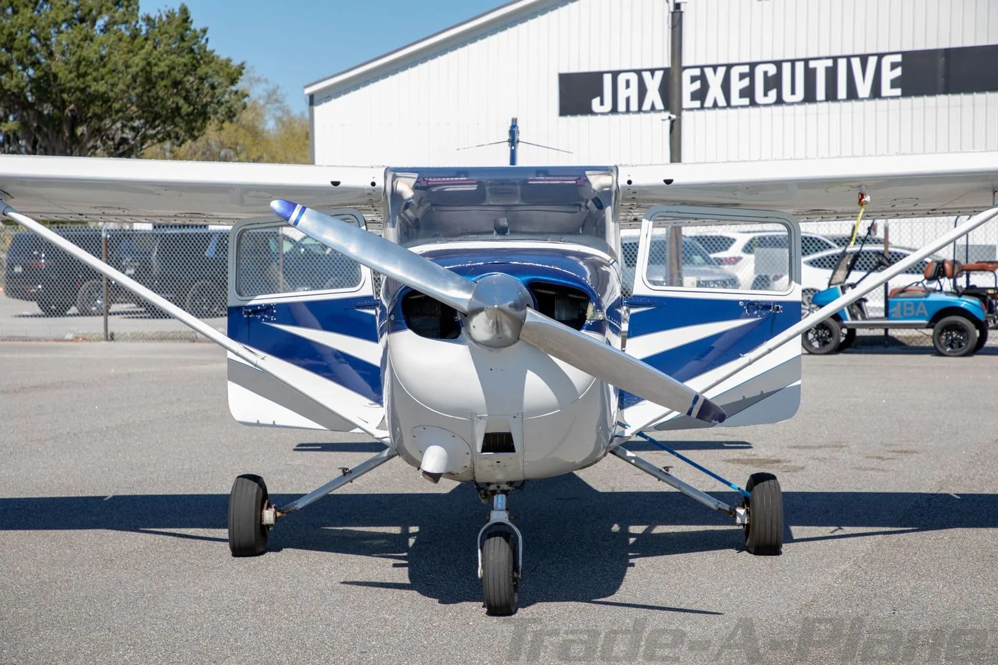 A front view of the N86ER aircraft, a white and blue Cessna 172, with its doors open, parked in front of a 'JAX EXECUTIVE' hangar.