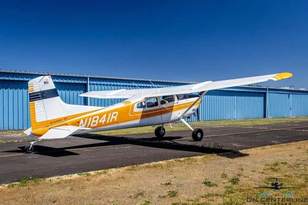 A rear-side view of a white and orange Cessna 185 Skywagon (N1841R) parked on an asphalt ramp.