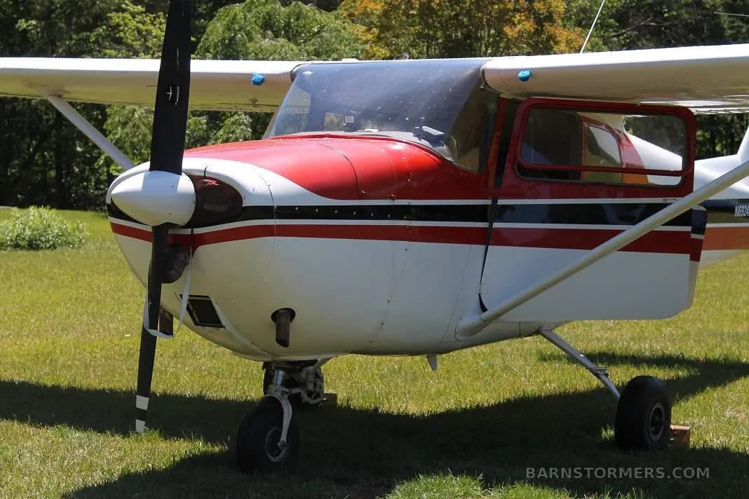 A close-up front view of the red and white Cessna 172, showing the propeller and nose gear on a grassy field.