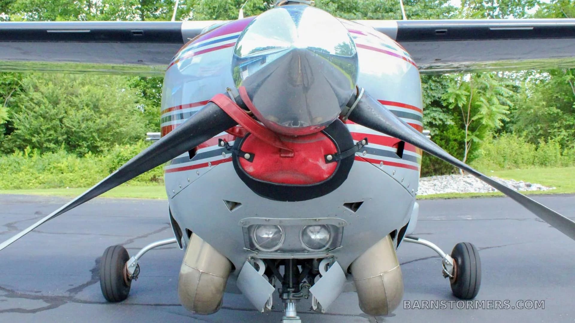 A close-up front view of a silver and red aircraft, showing its propeller, spinner, and engine cowling with landing lights.