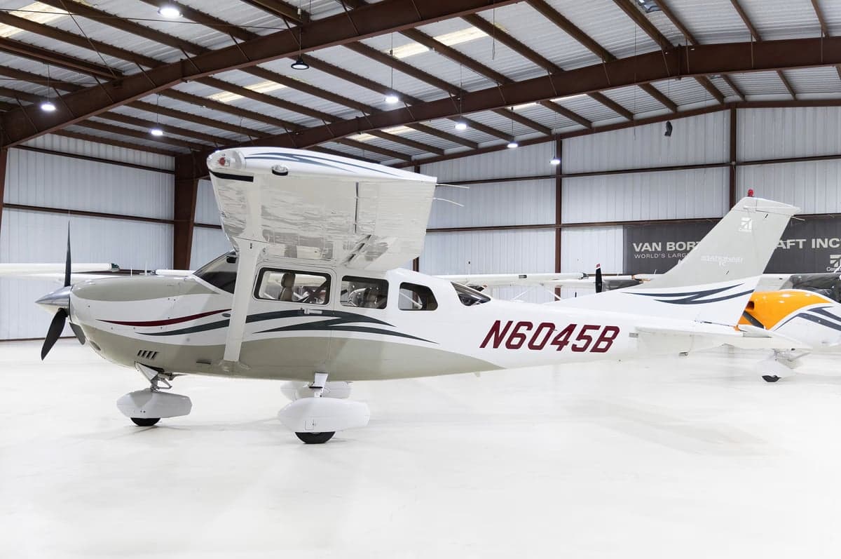 A side view of a white and grey Cessna Stationair TC (N6045B) with red and black accents, parked in a hangar.