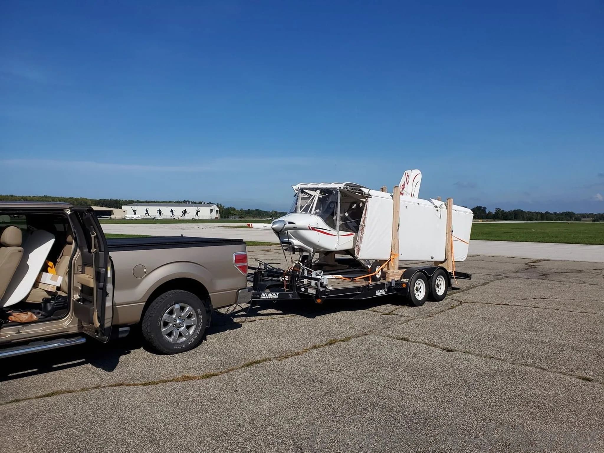 A disassembled white X-Air aircraft, registration N17XA, is loaded onto a trailer behind a tan pickup truck on an airfield.