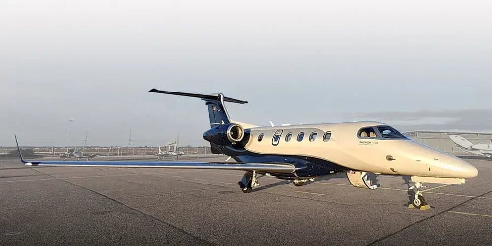 Side view of a tan and blue Phenom 300 aircraft on the tarmac.