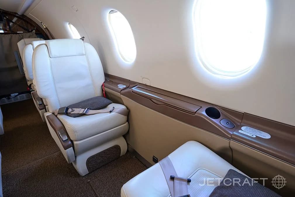 A view of light cream leather seats and large windows along the side of the aircraft cabin.